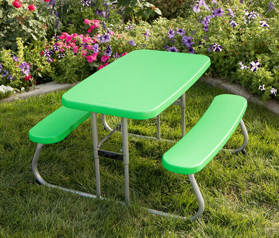 Ein grüner LIFETIME-Kinder-Picknicktisch »80094G« steht auf einer Wiese vor einem Blumenbeet.