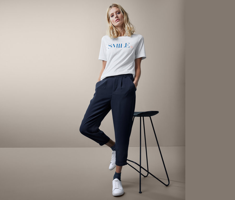 Frau posiert in einem weißen T-Shirt und einer Hose mit Bundfalte.
