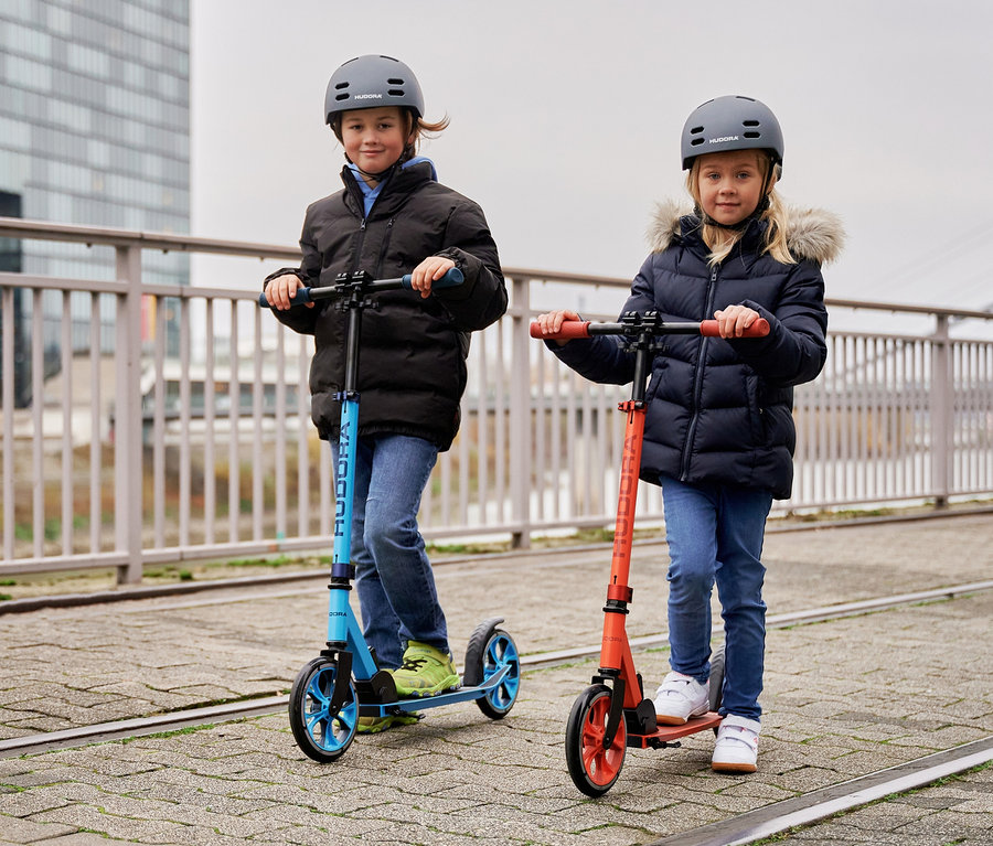 Kinder fahren auf dem Gehweg mit HUDORA Scootern »Up 200« in Rot und Blau.