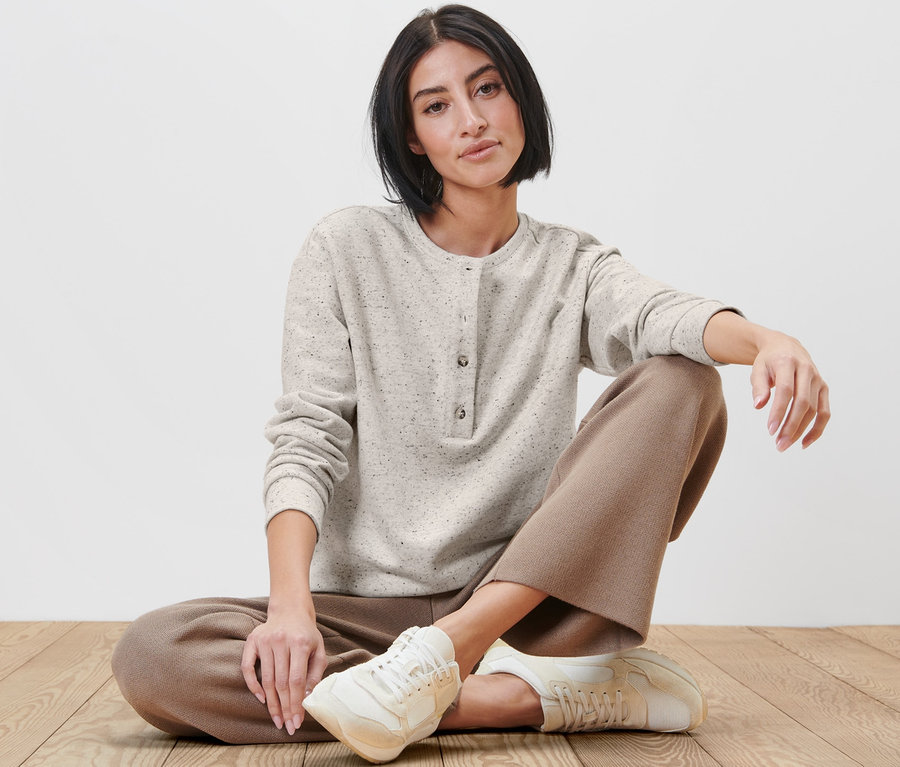 Frau sitzt in einem Sweatshirt mit Knopfleiste auf dem Boden.