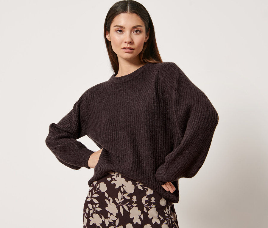 Frau posiert in Strickpullover und Rock mit Blumenmuster.