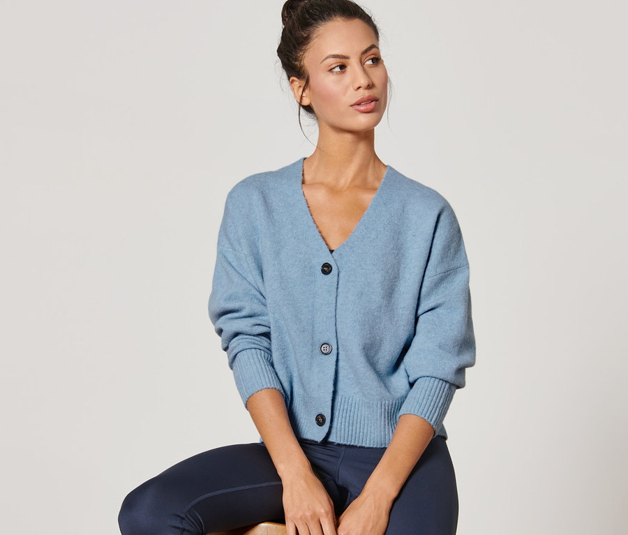 Frau sitzt auf einem Hocker und trägt einen blauen Grobstrick-Cardigan.