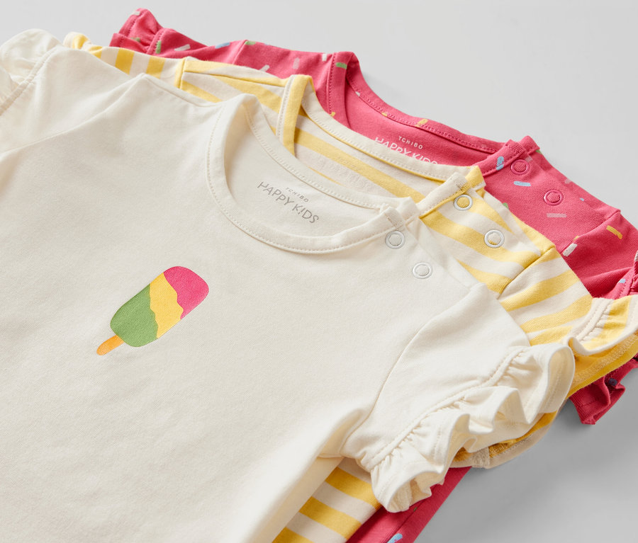 Drei Baby-T-Shirts: ein cremefarbenes mit Eis-Motiv, ein gelb gestreiftes und ein pinkfarbenes mit Muster.