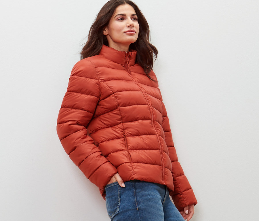 Frau posiert in orangefarbener Steppjacke.
