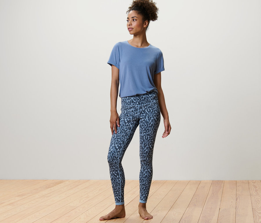 Eine Frau steht und trägt eine blau/hellblaue Wende-Sporttight und ein blaues T-Shirt.