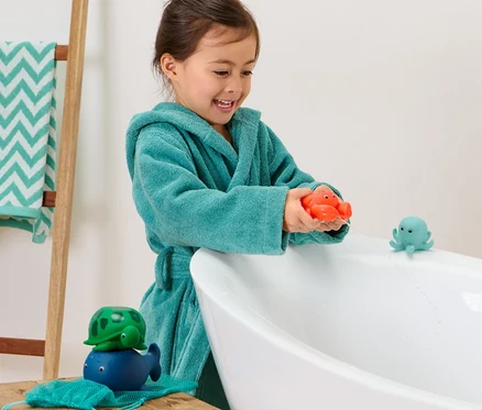 Ein Mädchen im Bademantel spielt mit 4 Wasserspritztieren in der Badewanne.