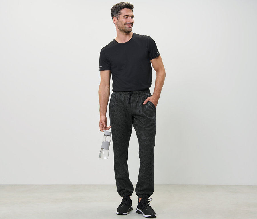 Mann im schwarzen T-Shirt hält eine Wasserflasche und trägt eine Sweathose.