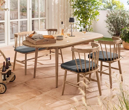 Outdoor-Szene mit ovalem Ausziehtisch, Dining-Stühlen mit Sitzpolster, Bank mit Sitzpolster, Barwagen und schwarzer LED-Akku-Outdoor-Tischleuchte.