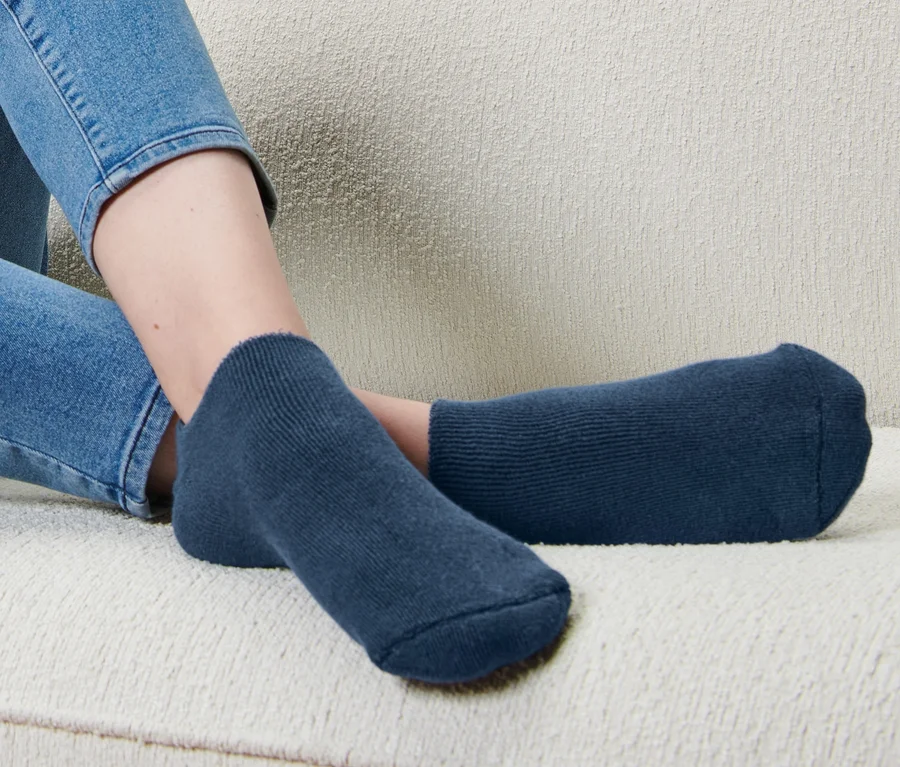 Eine Person sitzt auf einem Sofa und trägt dunkelblaue Fußpflegesocken.