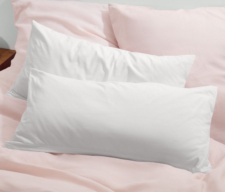 Zwei offwhite Jersey-Kopfkissenbezüge liegen auf einem Bett mit rosa Bettwäsche.