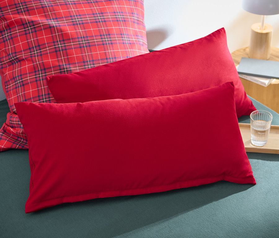 Zwei rote Microfaser-Flanell-Kopfkissenbezüge liegen auf einem Bett.