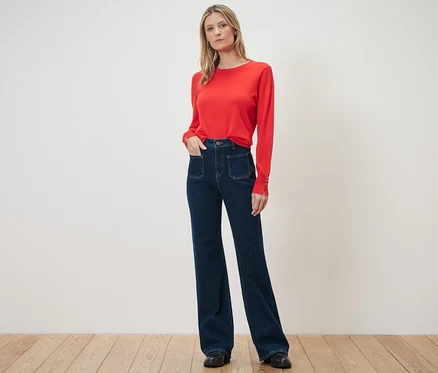 Eine Frau steht in einem roten Pullover und einer Flared Jeans – Fit »Cara«.