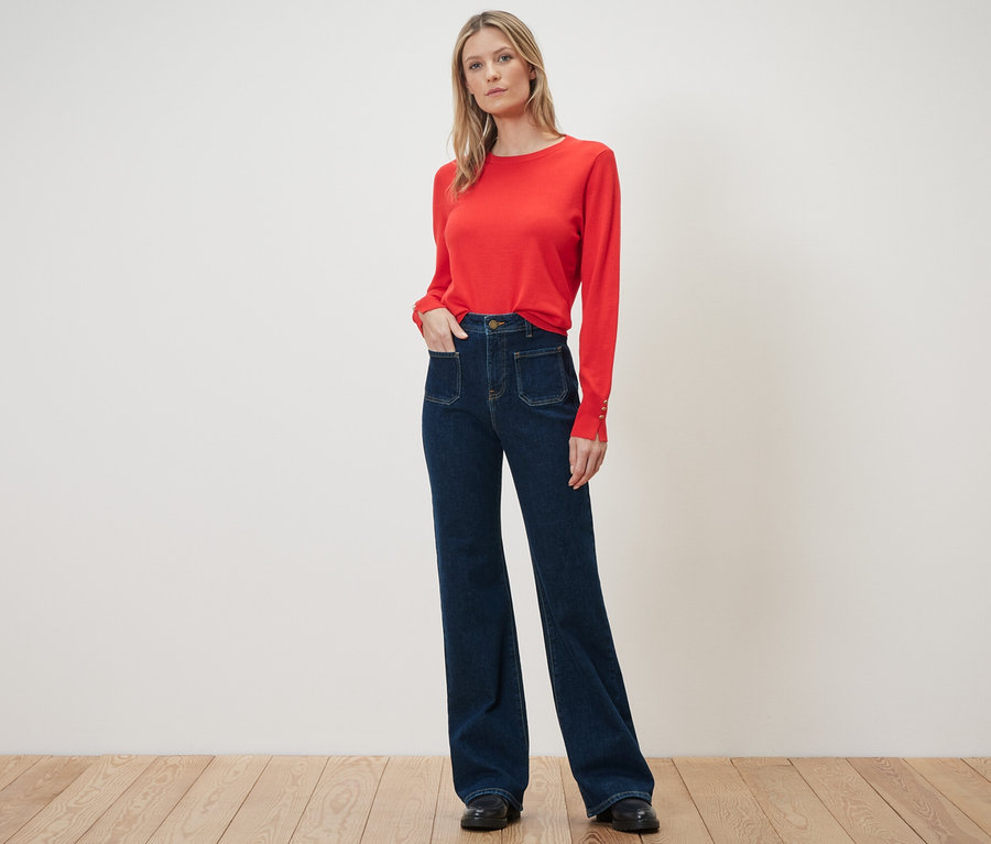 Eine Frau steht in einem roten Pullover und einer Flared Jeans – Fit »Cara«.