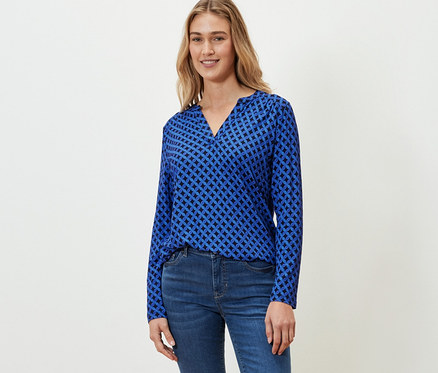 Eine Frau trägt ein kobaltblaues Blusenshirt mit Print und Jeans.