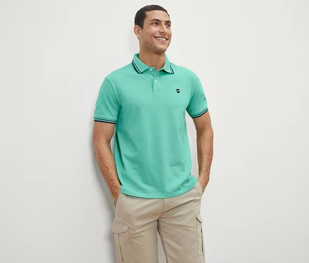 Ein Mann steht und lächelt, er trägt ein grünes Piqué-Poloshirt.