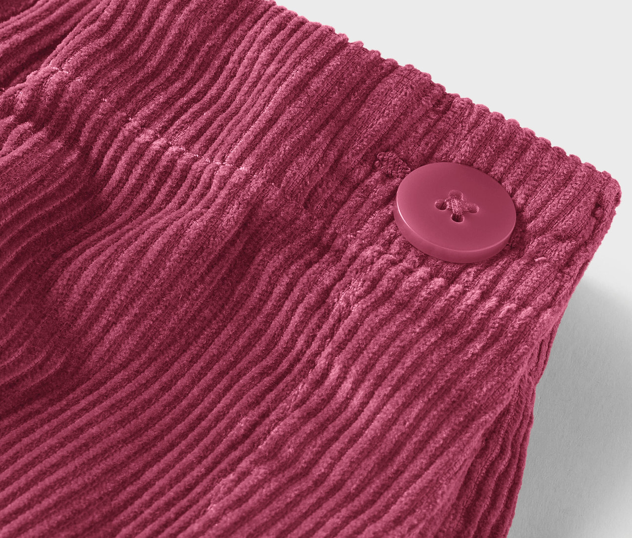 Detailaufnahme eines bordeauxroten Cordstoffs mit Knopf.