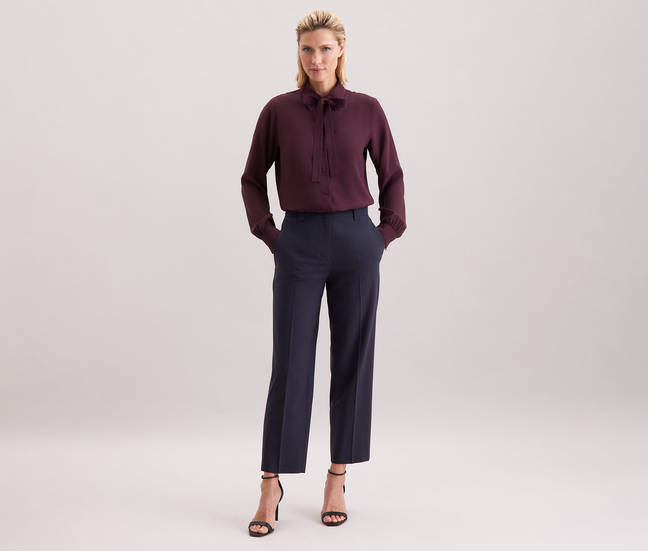 Frau mit dunkelroter Seidensticker Schluppenbluse aus Viskose, dunkler Hose und schwarzen Sandaletten.