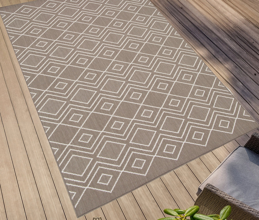 Ein brauner, faltbarer Outdoor-Teppich »Diamond Rhythm« mit weißem geometrischen Muster liegt auf einer Holzterrasse.