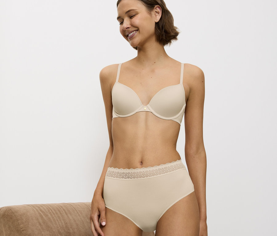 Eine lächelnde Frau trägt einen beigen BH und Höschen mit Spitze.