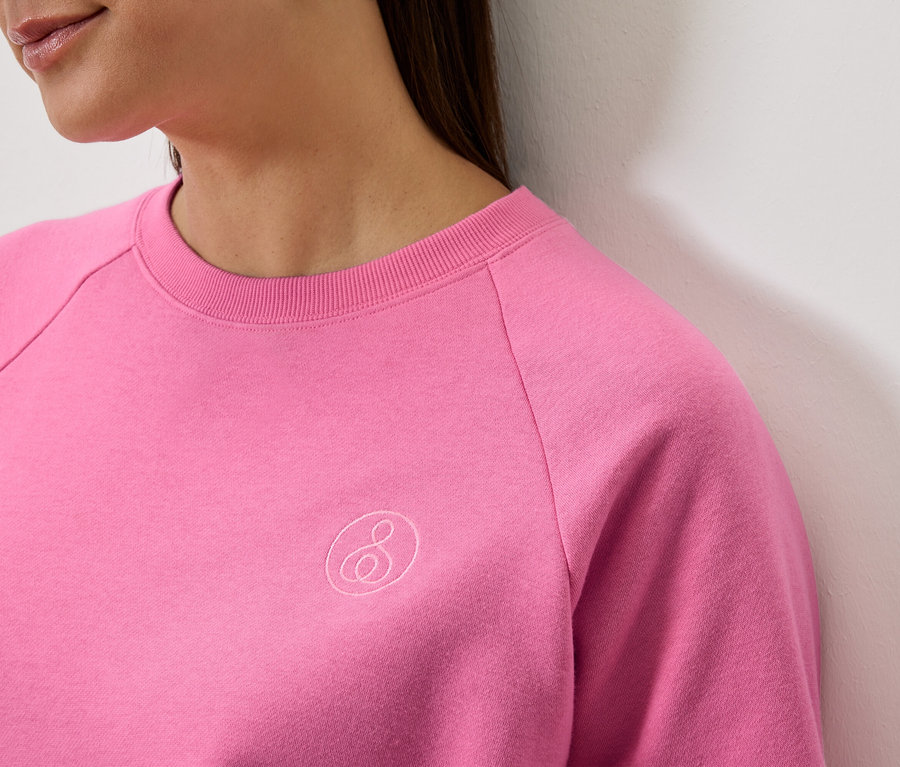 Detailaufnahme einer Frau, die ein pinkes Langarm-Sweatshirt mit Logo trägt.