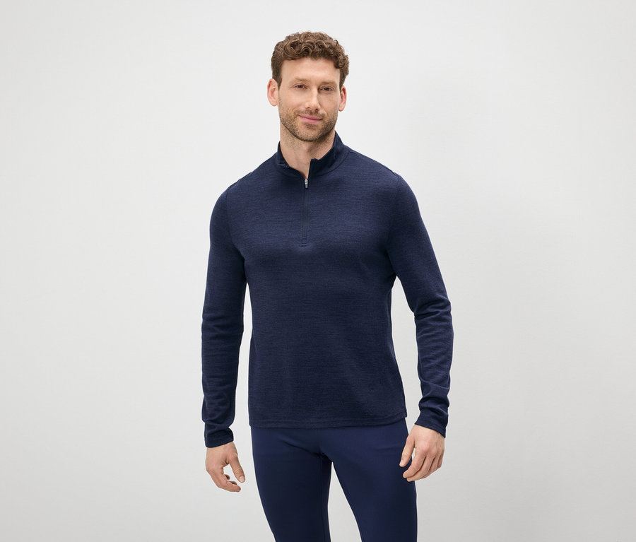 Mann mit braunen Haaren und Bart trägt einen blauen Pullover mit Reißverschluss und blaue Hosen.