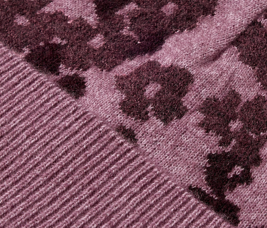 Detailaufnahme eines lilafarbenen Strickpullovers mit Blumenmuster.