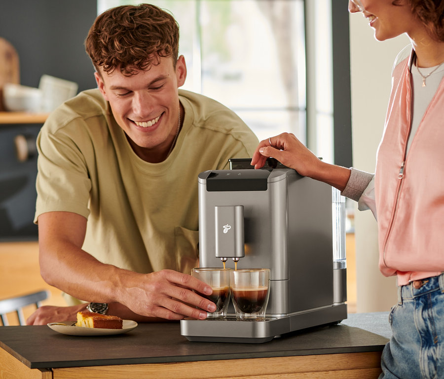 Ein Mann schaut zu, wie Kaffee aus einem »Esperto2 Caffè« Kaffeevollautomaten in Titanium Silver in zwei Gläser gegossen wird.