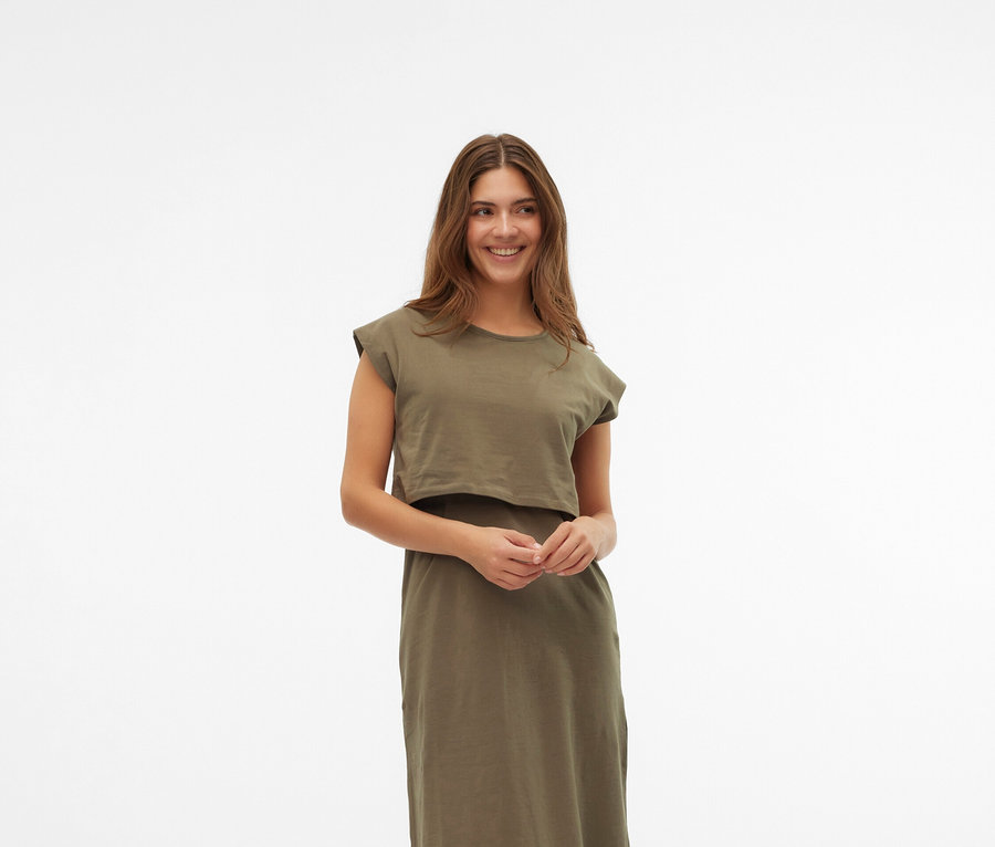 Frau trägt ein khakifarbenes Kleid und cremefarbene Mary Jane Schuhe vor einem weißen Hintergrund.