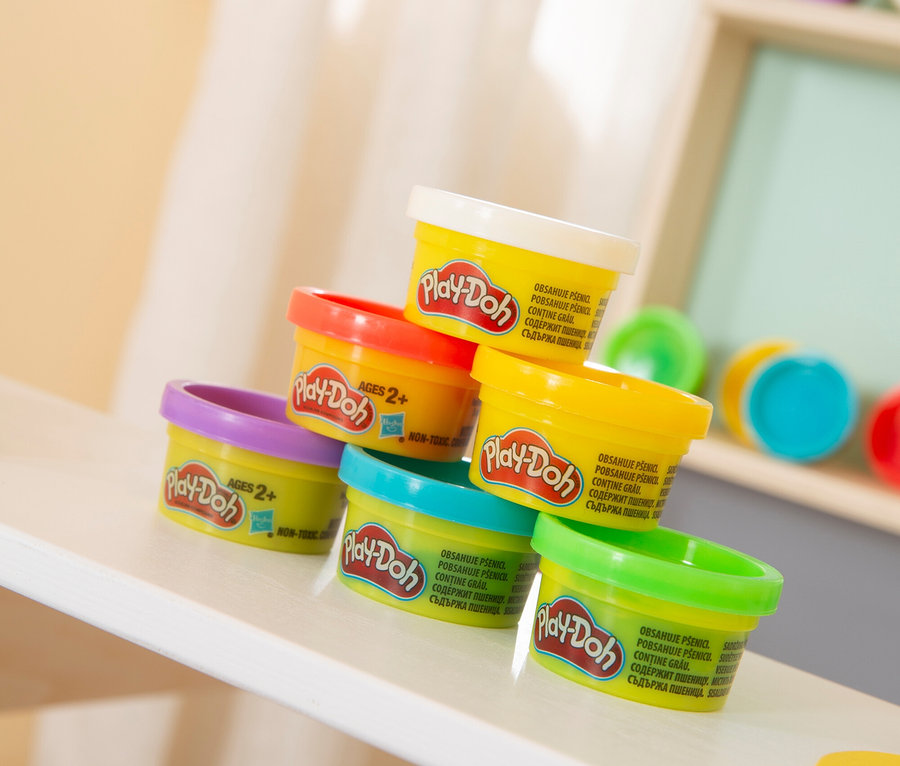 Ein Stapel aus sechs bunten Play-Doh Dosen steht auf einem Regal.