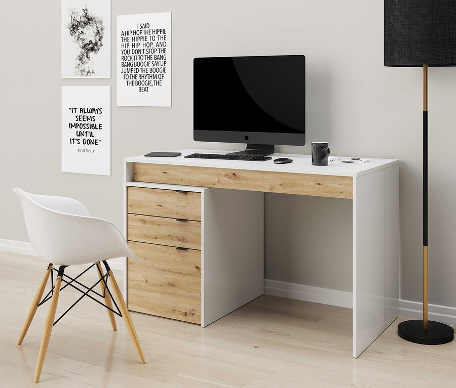 Schreibtisch mit Computermonitor, Tastatur und Schreibtischlampe. An der Wand hängen drei gerahmte Poster.