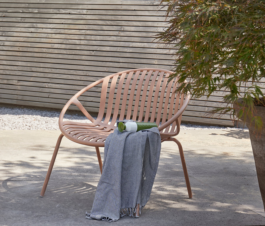 Ein rosafarbener Stuhl steht draußen mit einer Decke, einer Tasse und einer Flasche darauf.