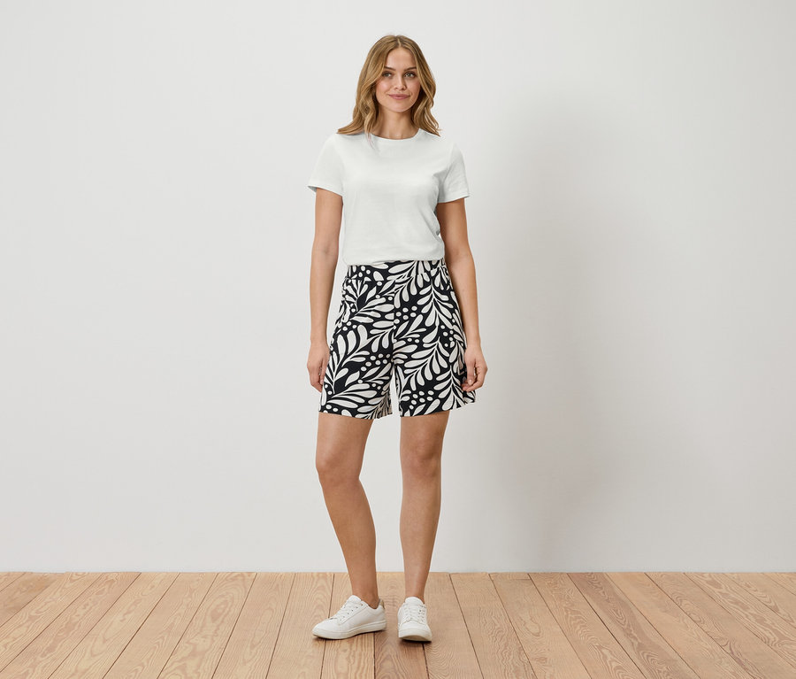 Frau steht in weißem T-Shirt und gemusterten Shorts.