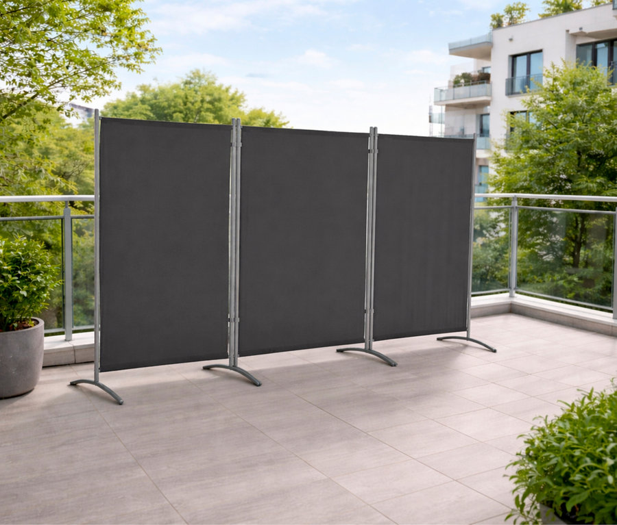 Anthrazitfarbene, dreiteilige Leco Stellwand auf einem Balkon mit Pflanzen und einem Gebäude im Hintergrund.