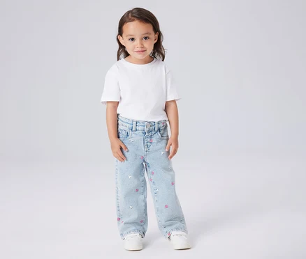 Mädchen mit weißem T-Shirt und hellblauen Jeans mit Herz- und Mausmuster.