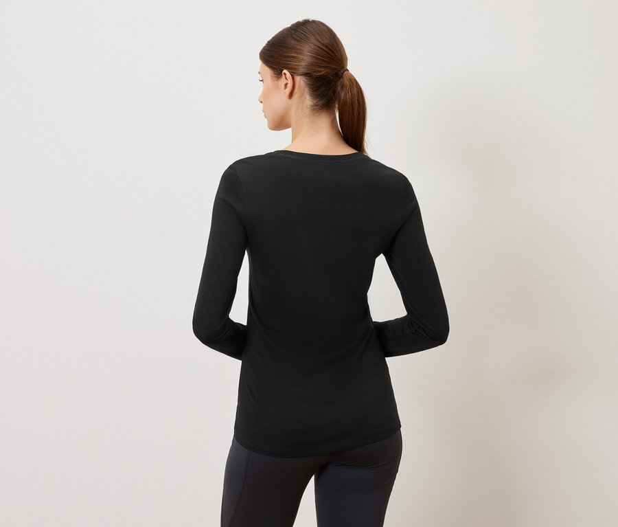 Rückansicht einer Frau mit einem schwarzen Langarmshirt und schwarzen Leggings vor einem neutralen Hintergrund.