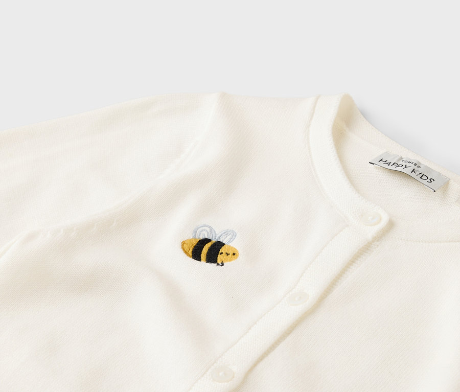 Nahaufnahme einer weißen Strickjacke mit Knopfleiste und gestickter Biene.