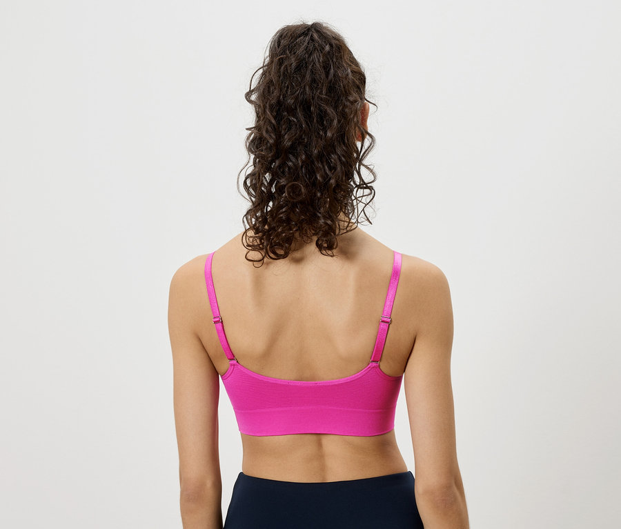 Rückansicht einer Frau mit hochgesteckten lockigen Haaren, die einen pinkfarbenen Sport-BH und marineblaue Leggings trägt.