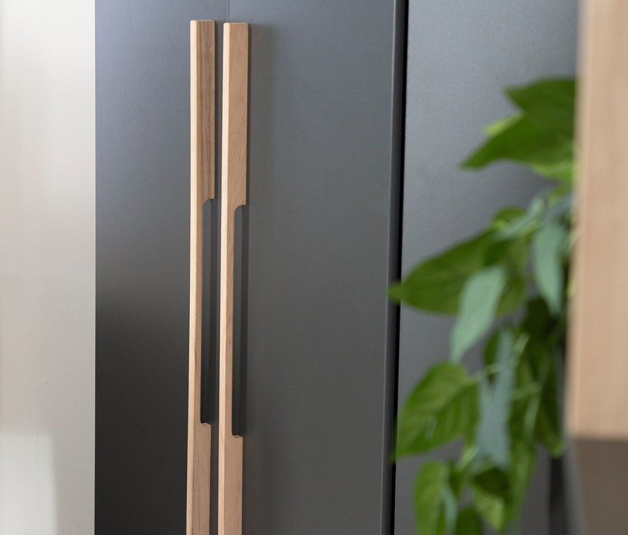 Detailansicht eines Roba Eckschranks »Marvin« mit hölzernen Griffen und einer Pflanze im Hintergrund.