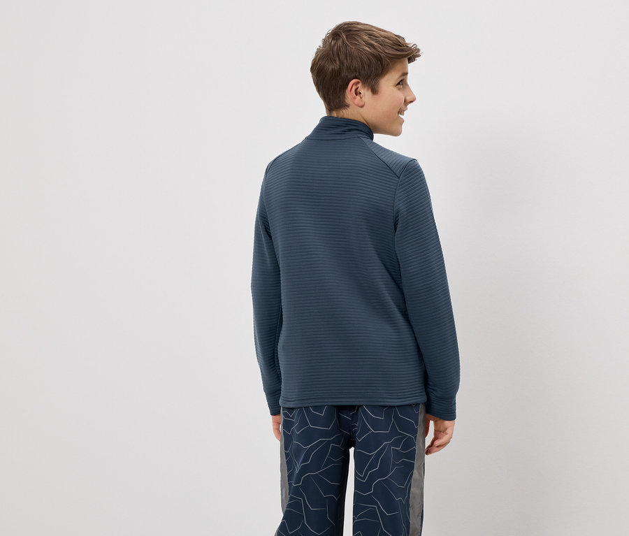 Teenager von hinten, trägt blaues, gestreiftes Oberteil mit Reißverschluss und gemusterte Hose vor einem weißen Hintergrund.