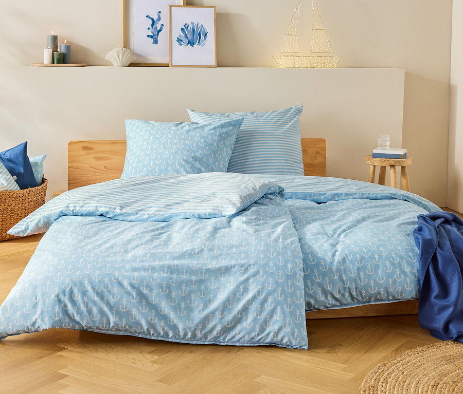 Ein blau-weißes Bett mit Ankermuster steht in einem Schlafzimmer. Auf dem Nachttisch steht ein Glas Wasser.