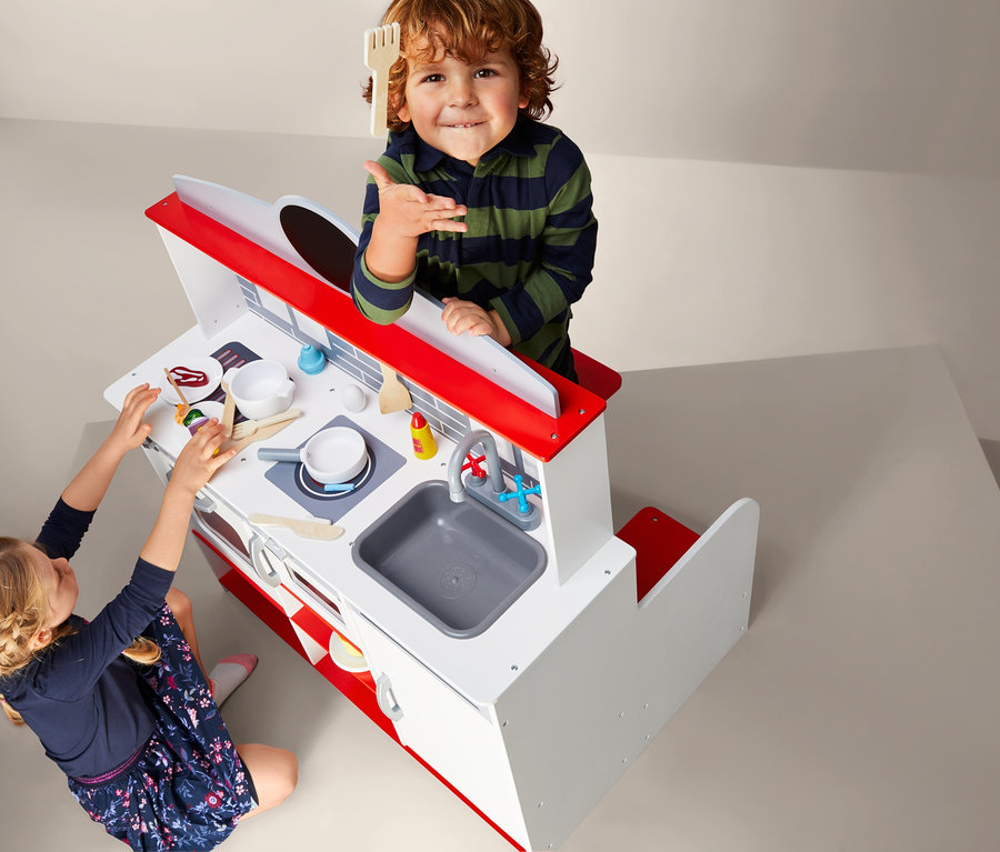 Kinder spielen mit der 2-in-1-Restaurant-Spielküche. Ein Junge hält eine Holzzgabel, während ein Mädchen mit Essen auf der Küchenzeile spielt.