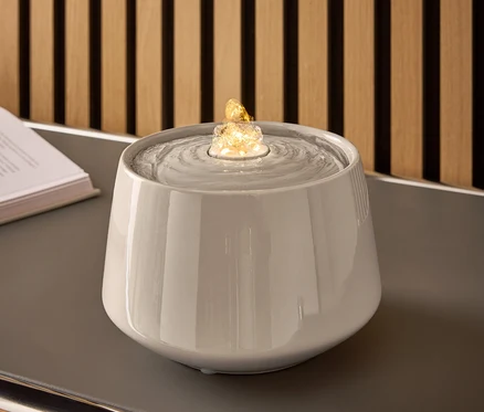 Grauer Keramikbrunnen mit Wasser und beleuchtetem Stein auf einem grauen Tisch.
