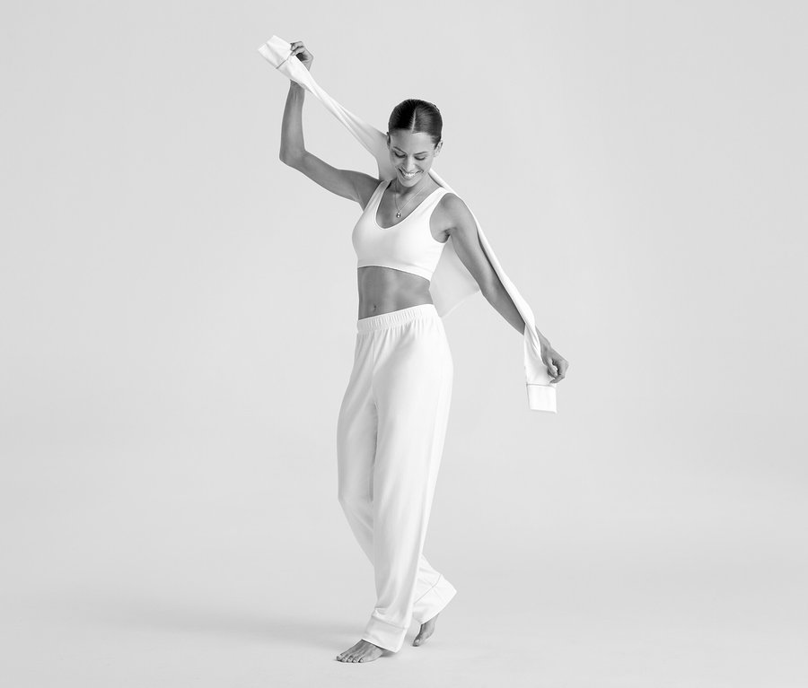 Lächelnde Frau in einem cremefarbenen Seamless-Bustier und Hose, die ein Tuch über dem Kopf hält.