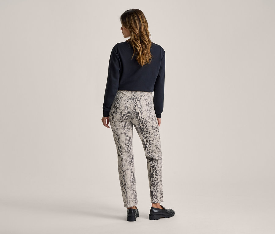 Frau von hinten, die ein dunkles Langarmshirt, eine helle Hose mit Schlangenmuster und schwarze Loafer trägt.