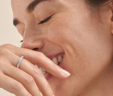 Lächelnde Frau mit geschlossenen Augen trägt eine silberne Kette mit Zirkonia, silberne Ohrstecker mit Zirkonia und zwei silberne Ringe Memoire mit Zirkonia.