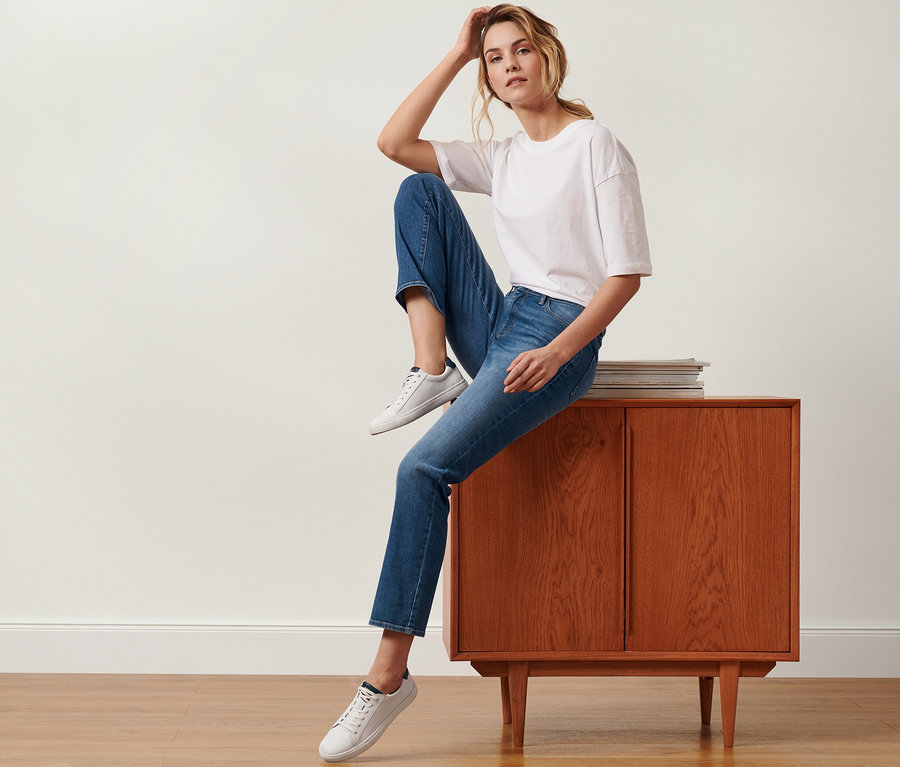 Eine Frau sitzt auf einem braunen Schrank und trägt eine Straight-Denim »Fit Kira« in Midblue Denim.