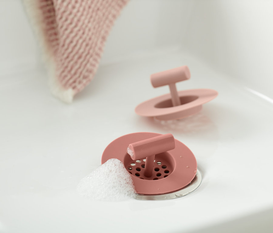 Zwei Abflusssiebe aus Silikon im Waschbecken, eines mit Schaum.
