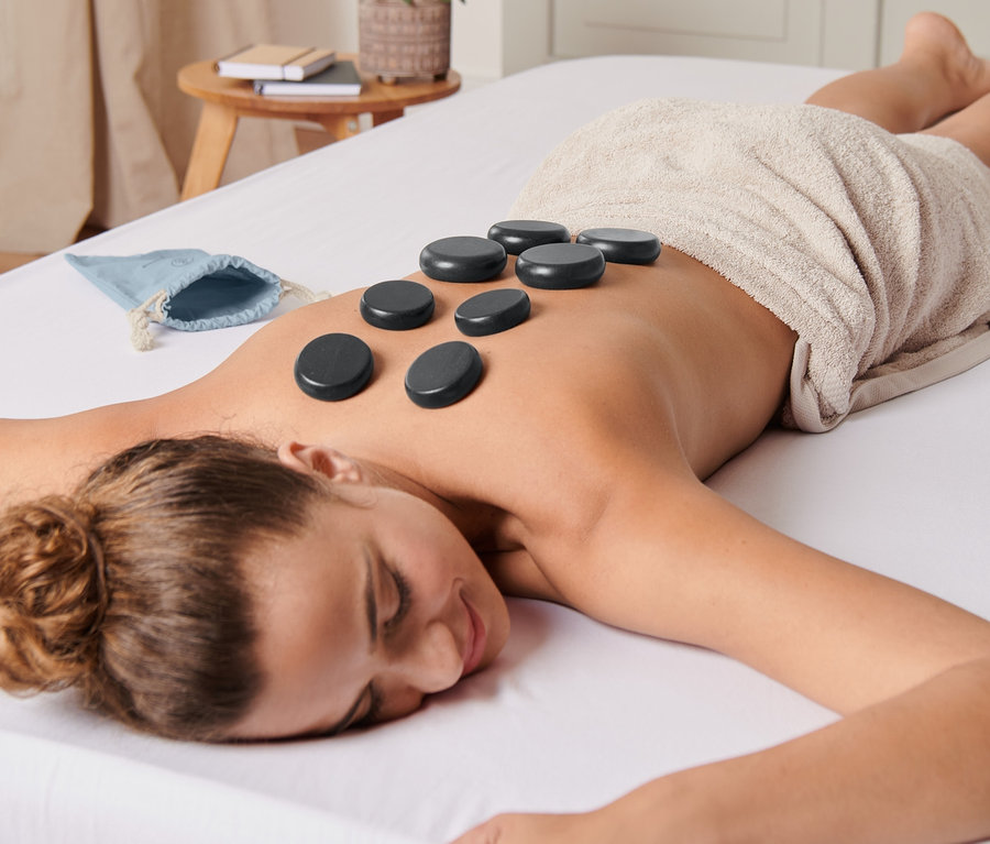 Frau liegt mit Hot Stones Massageset auf dem Rücken.