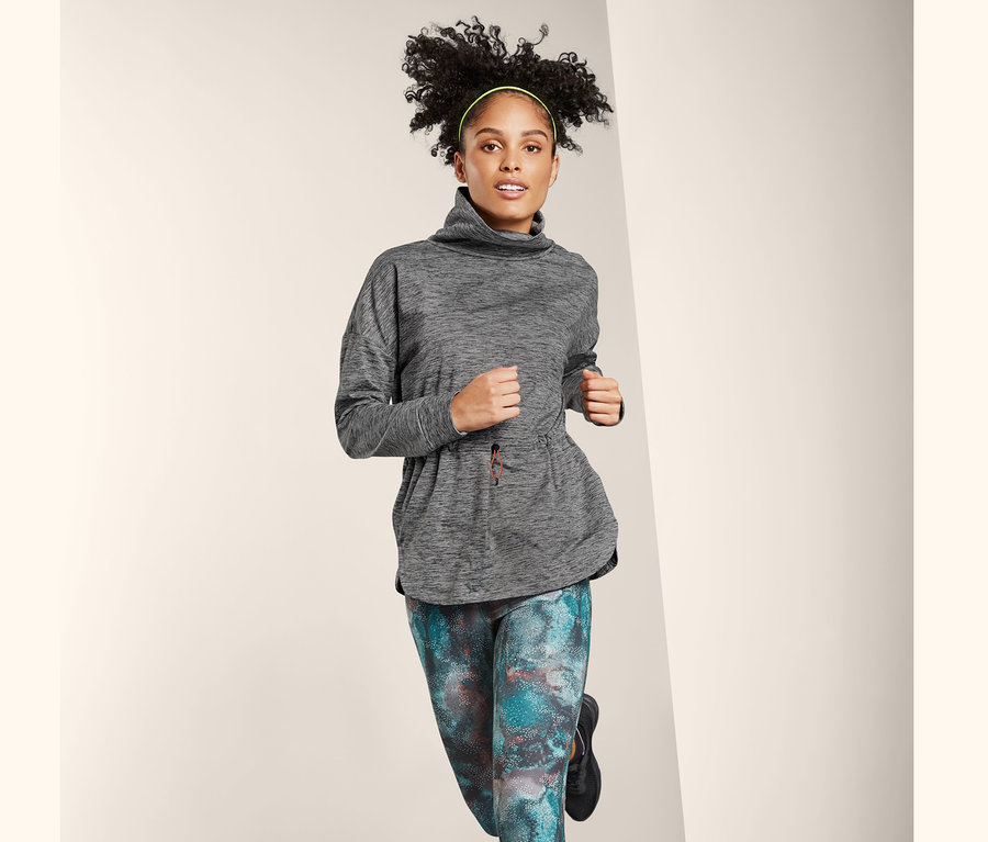 Eine Frau im Laufschritt trägt einen Thermo-Funktionssweater, bunte Leggings und schwarze Turnschuhe.