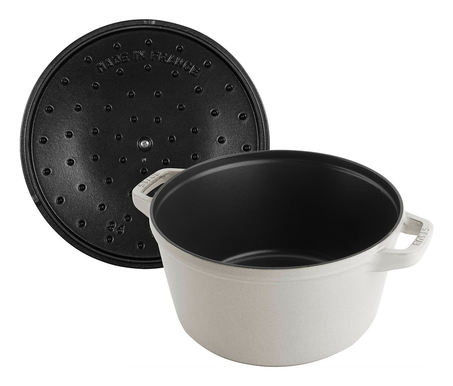 Ein weißer STAUB Kochtopf La Cocotte mit schwarzer Innenseite und einem Deckel daneben.